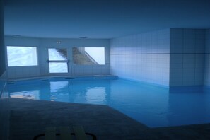 Une piscine intérieure avec des murs et des fenêtres recouverts de carreaux.