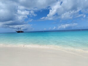 Una playa con aguas turquesas cristalinas, un barco a lo lejos y una orilla arenosa.