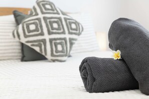 A neatly made bed with a rolled gray towel and a white pillow with a geometric pattern.