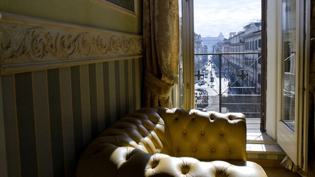 A room with a large window, a plush sofa, and a view of a cityscape. - Upper View Suite (Rome)