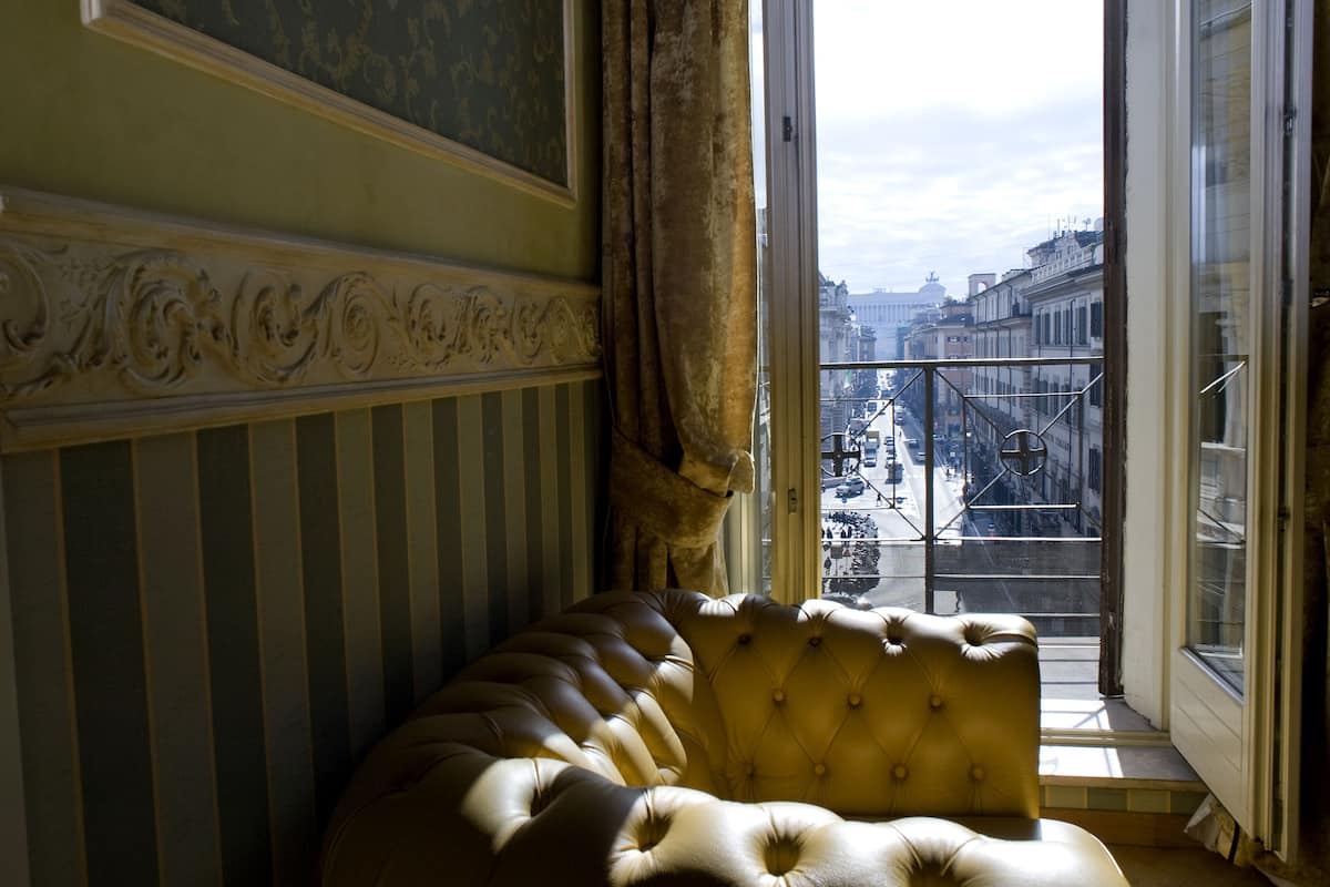 A room with a large window, a plush sofa, and a view of a cityscape.