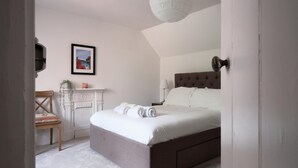 Ein Schlafzimmer mit einem großen Bett, einem Sessel, einem Schreibtisch mit Lampe und einem gerahmten Bild an der Wand.