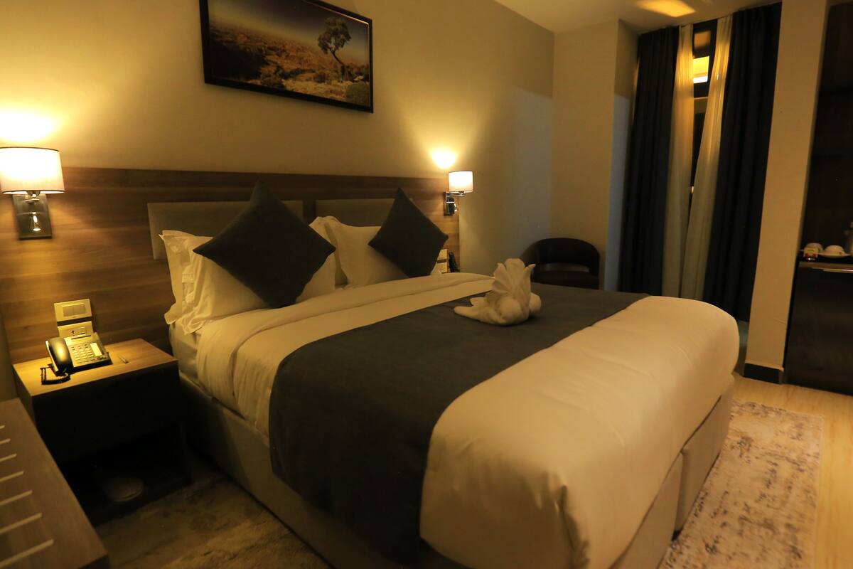 A hotel room with a large bed, bedside lamps, a telephone, and a painting on the wall.