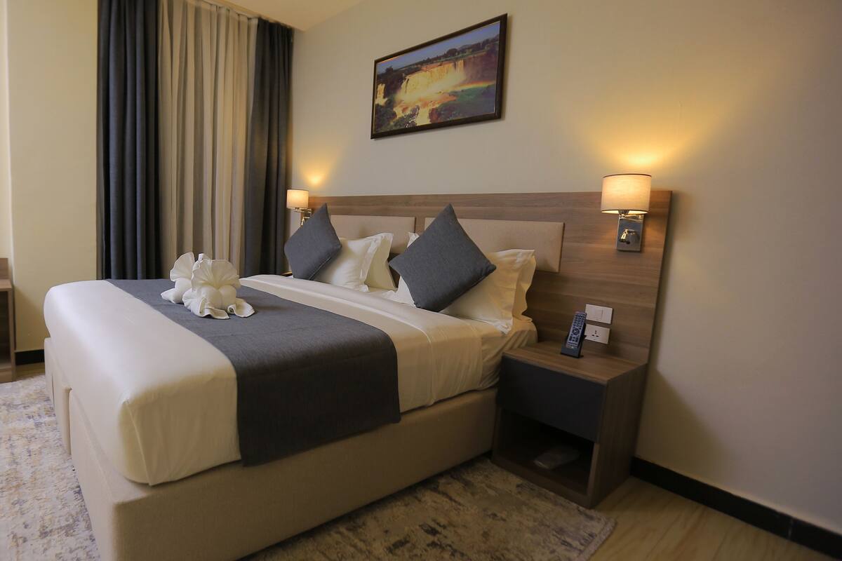 A hotel room with a large bed, two bedside lamps, a nightstand with a remote control, and a painting on the wall.