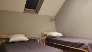 Een kleine, eenvoudige kamer met twee eenpersoonsbedden, een tafeltje en een dakraam.