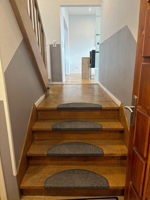A staircase with wooden steps and carpeted risers leading to a room with a door on the right.