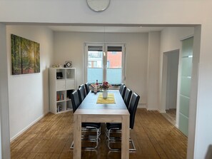 A dining area with a wooden table, black chairs, a white cabinet, and a painting on the wall.