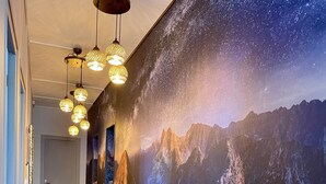 Un pasillo con piso de madera, lámparas colgantes y un gran mural en la pared que muestra un paisaje montañoso.