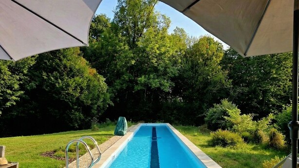 Una piscina con muelle de madera, sillas de descanso y sombrillas.