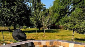 Un jacuzzi con diseño de baldosas geométricas, rodeado de un borde de piedra, situado en un jardín con árboles y un objeto esférico decorativo.