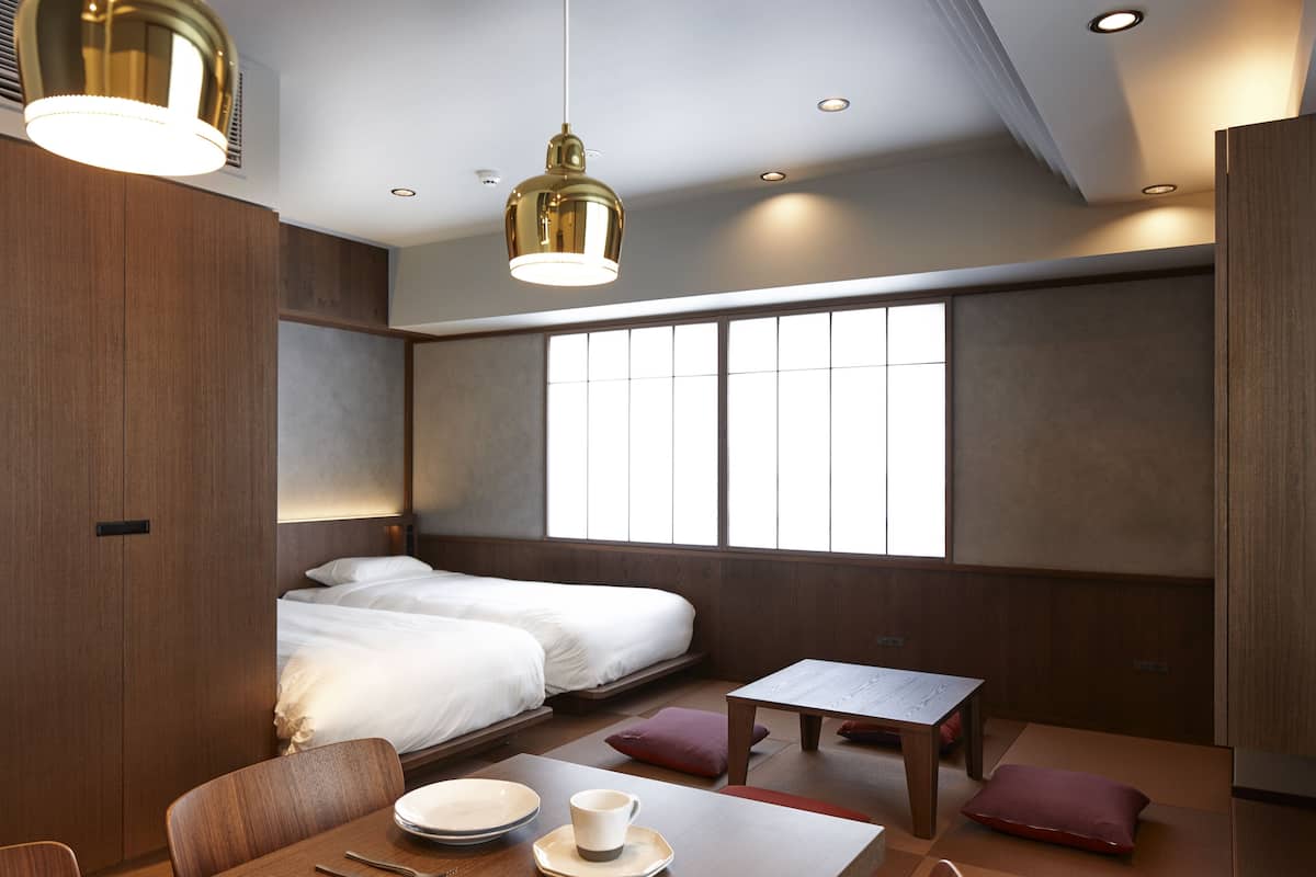 A modern hotel room with a bed, a dining table with plates and a cup, and a window with blinds.