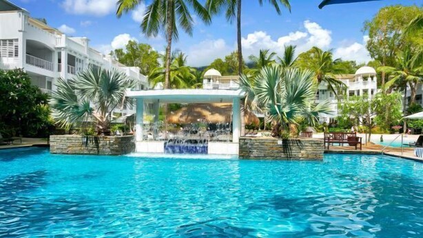A clear blue pool with a waterfall feature, surrounded by palm trees and lounge chairs.