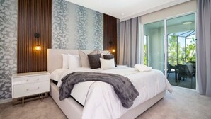 Quarto moderno com uma cama grande, uma mesa de cabeceira e uma porta de vidro que dá para uma área externa.