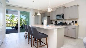 Uma cozinha moderna com uma ilha grande, banquetas e vista para uma piscina.