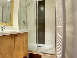 Une salle de bain avec une douche à parois de verre, un meuble-lavabo en bois et un lavabo blanc.