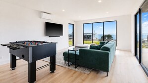 A modern living room with a foosball table, a flat-screen TV, a green sofa, and large windows offering a view of the sea. - The Bay View San Remo by Ready Set Stay (San Remo)