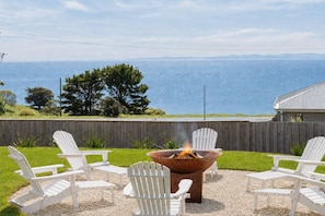 A patio with a fire pit and white Adirondack chairs overlooking a body of water. - The Bay View San Remo by Ready Set Stay (San Remo)