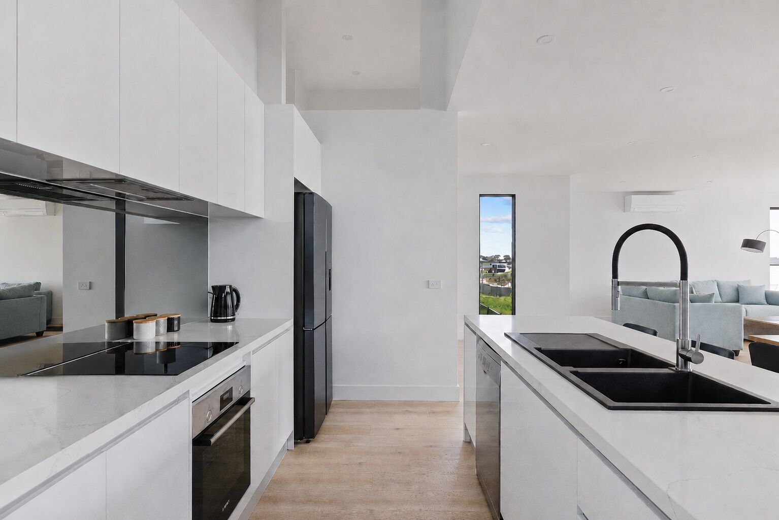 A modern kitchen with a black refrigerator, stainless steel appliances, and a view to the outside.