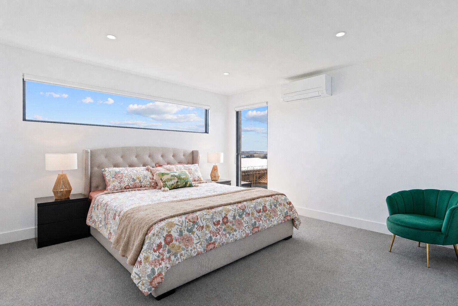 A modern bedroom with a large bed, two bedside tables with lamps, a green armchair, and a large window with a view.