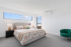 A modern bedroom with a large bed, two bedside tables with lamps, a green armchair, and a large window with a view. - The Bay View San Remo by Ready Set Stay (San Remo)