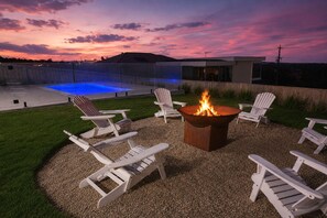 An outdoor seating area with a fire pit and chairs, a pool, and a modern building in the background. - The Bay View San Remo by Ready Set Stay (San Remo)