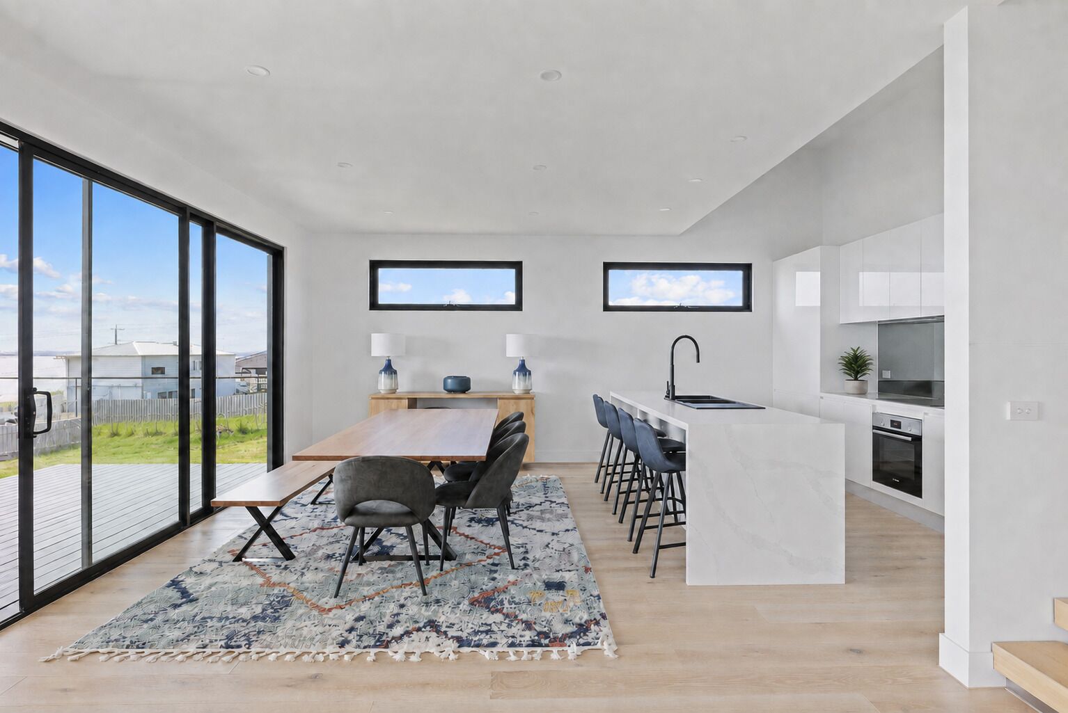 A modern kitchen with a dining area, large windows, and a view of the outdoors.