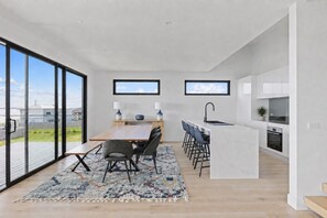A modern kitchen with a dining area, large windows, and a view of the outdoors. - The Bay View San Remo by Ready Set Stay (San Remo)