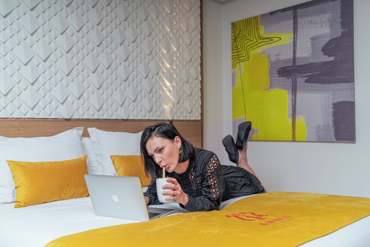 A hotel room with a bed, a laptop, and a mug.