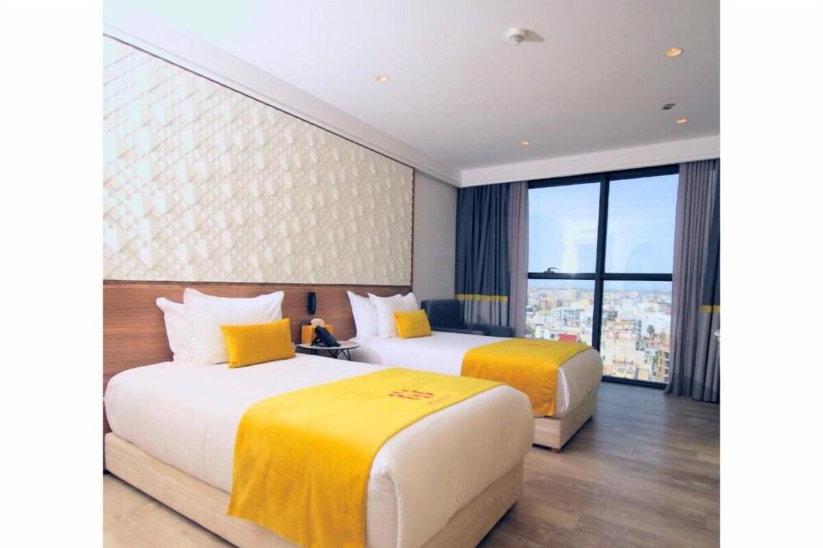 A hotel room with two beds, a city view, and a modern design.