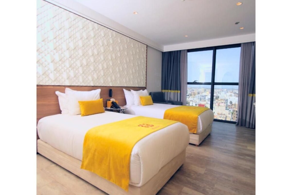 A hotel room with two beds, a city view, and a modern design.