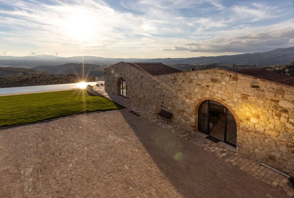 A stone building with a paved courtyard, a bench, and a view of distant hills.