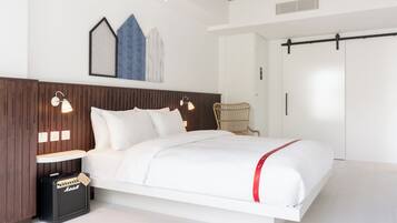 Un dormitorio moderno con una cama blanca, cabecero de madera, dos lámparas de noche, un amplificador Marshall y una obra de arte colgada en la pared.