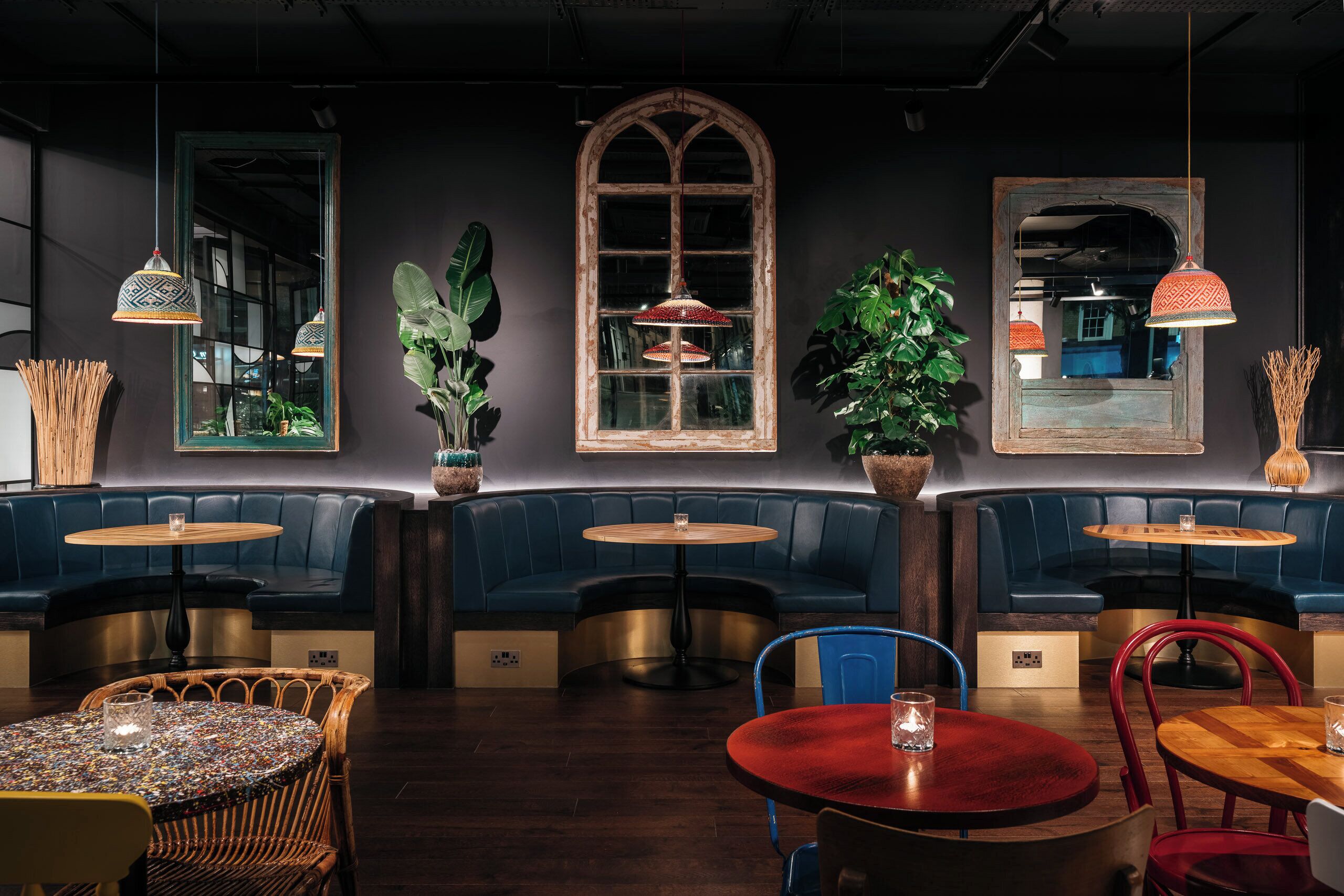 A restaurant with round tables, blue booths, and hanging pendant lights.
