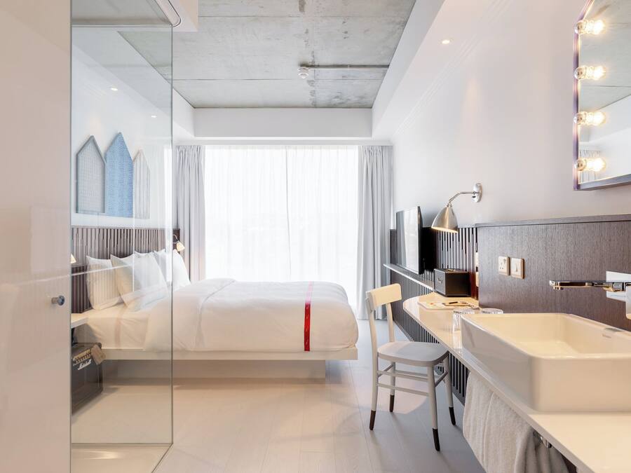 Habitación de hotel moderna con una cama grande, un separador de vidrio, un baño con bañera y un espejo amplio con luces.