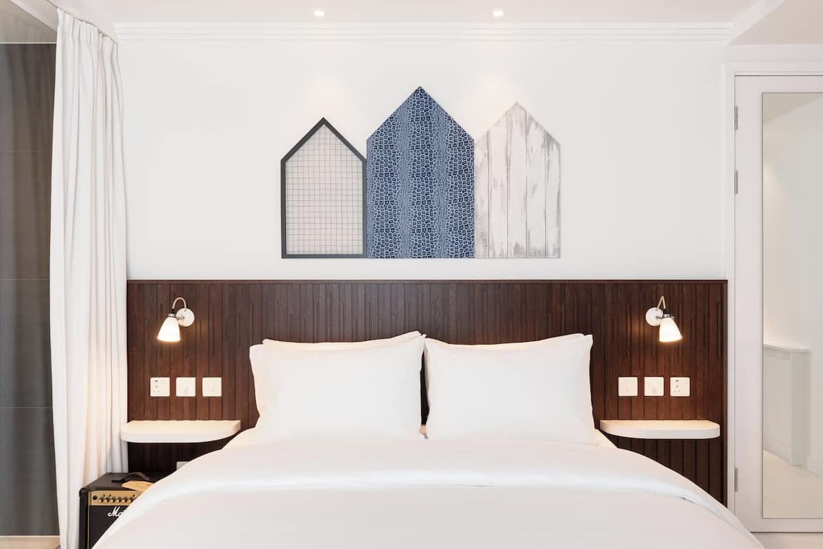 A neatly made bed with a headboard, two bedside tables with lamps, and a wall with three decorative panels.