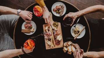 Una mesa redonda con diversos alimentos y bebidas, rodeada de gente.