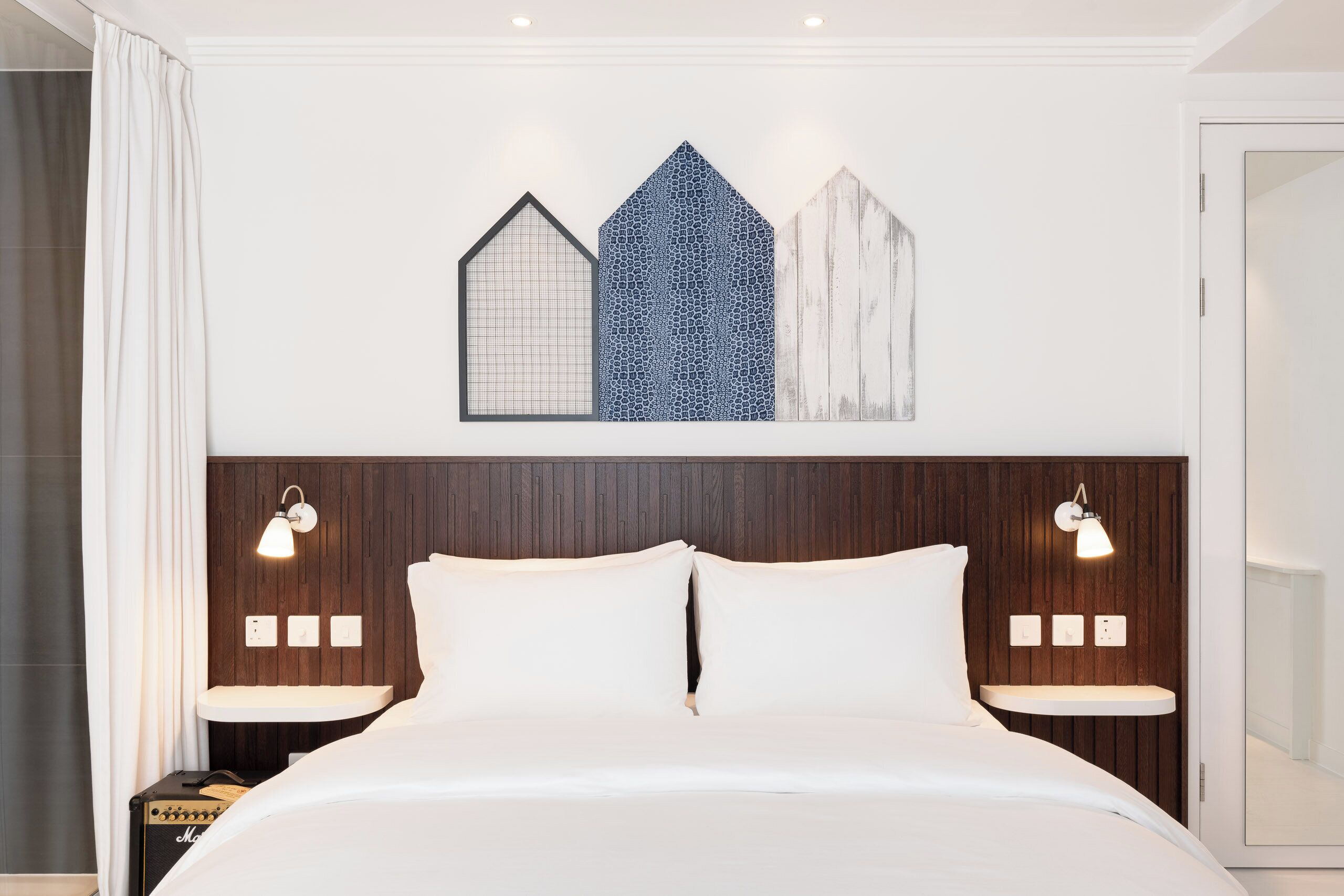 A neatly made bed with a headboard, two bedside tables with lamps, and a wall with three decorative panels.