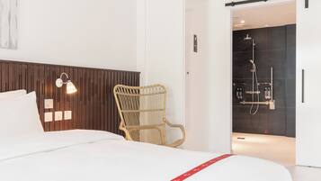 A hotel room with a bed, a wicker chair, a wall-mounted light, and a shower area.