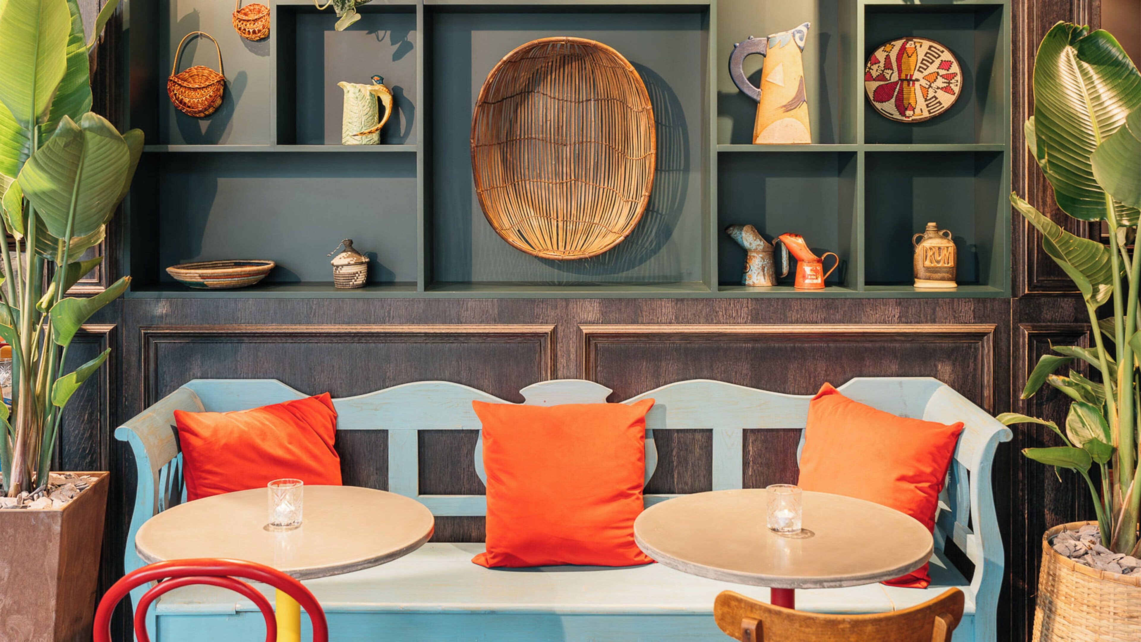 Un área de descanso con un banco y dos mesas redondas, rodeada de estanterías con diversos objetos decorativos.