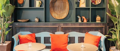 Un área de descanso con un banco y dos mesas redondas, rodeada de estanterías con diversos objetos decorativos.