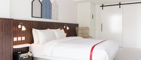 A modern bedroom with a bed, two bedside lamps, a wall-mounted artwork, a wooden headboard, and a Marshall amplifier on the floor.