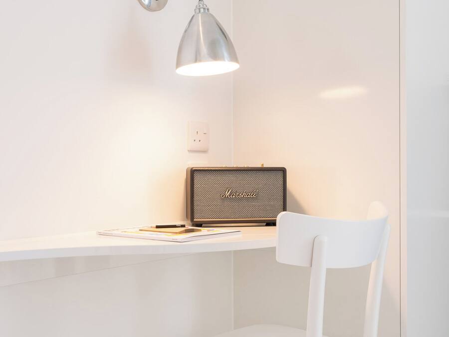 Uma escrivaninha branca com um laptop, um objeto emoldurado e uma luminária.