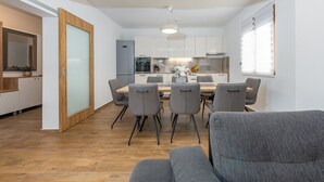 Une cuisine moderne avec des meubles blancs, une table à manger entourée de six chaises et un canapé gris au premier plan.