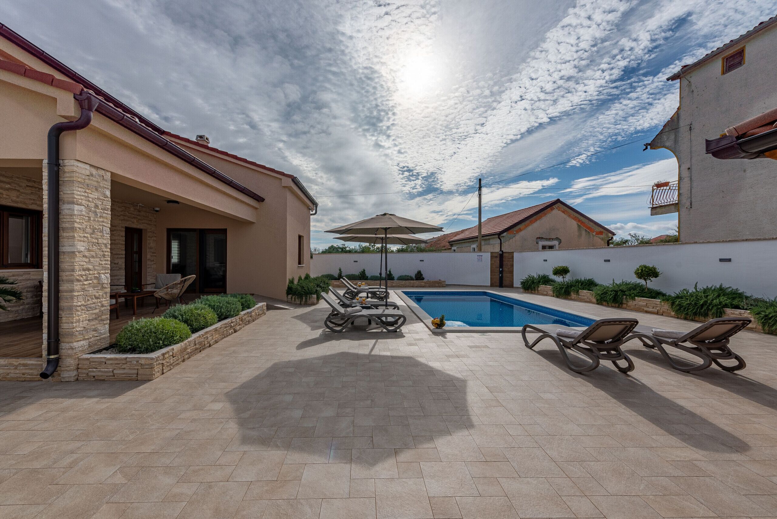 A backyard with a swimming pool, lounge chairs, and a covered patio area.