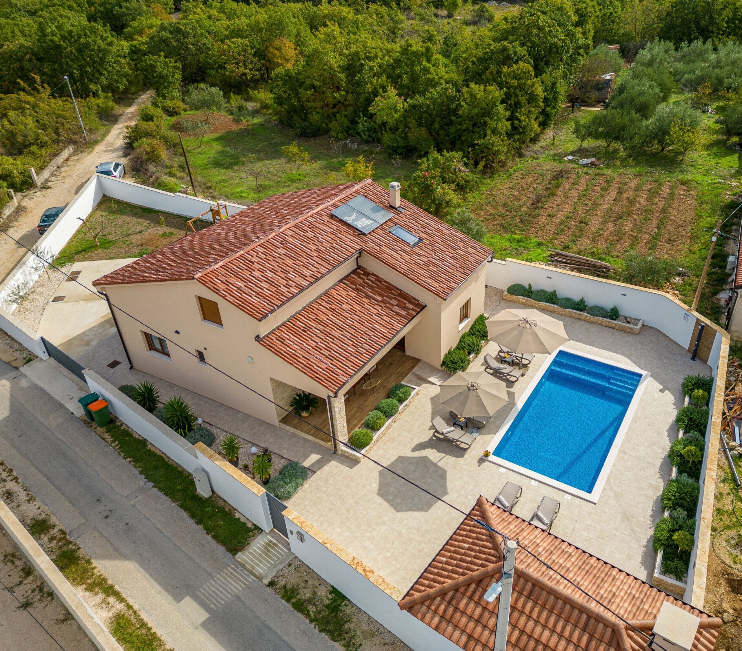 A two-story house with a swimming pool, a covered patio, and a garden.