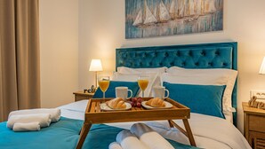 Une chambre d’hôtel avec un lit, un plateau avec des croissants et du jus, et un tableau représentant des voiliers accroché au mur.