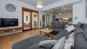 Un salon moderne avec un grand canapé d’angle, un téléviseur à écran plat et une table basse en bois.