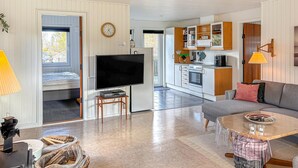Ein modernes Wohnzimmer mit Flachbildfernseher, einer Couch, einem Esstisch und einer Küchenzeile mit Schränken und Herd.