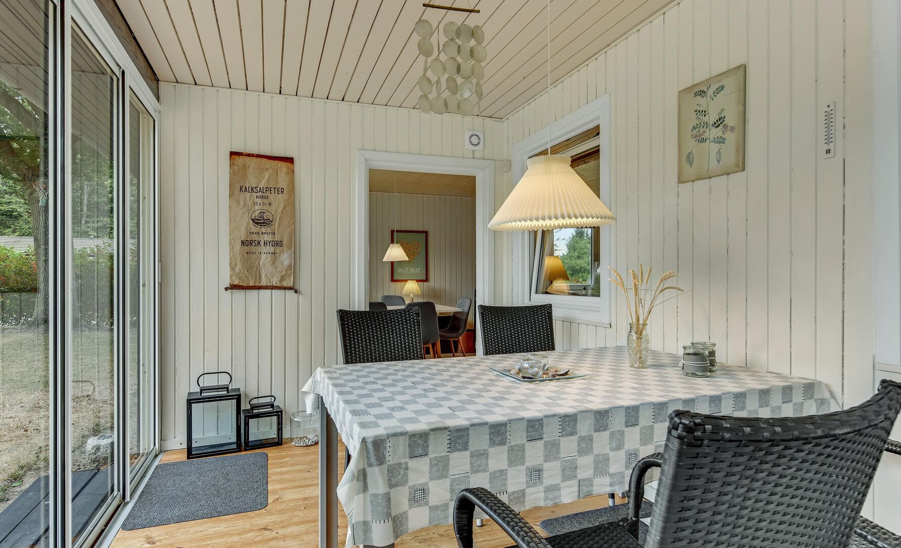 En hyggelig spiseplads med dug i tern, fletstole og en bordlampe.