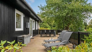 Eine Holzterrasse mit Sitzgelegenheiten im Freien und ein schwarzes Gebäude mit Fenstern.